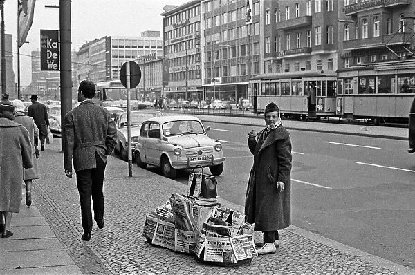 Newspaper vendor on the Kufurstendamm, Berlin, keeps herself warm with a cup of coffee