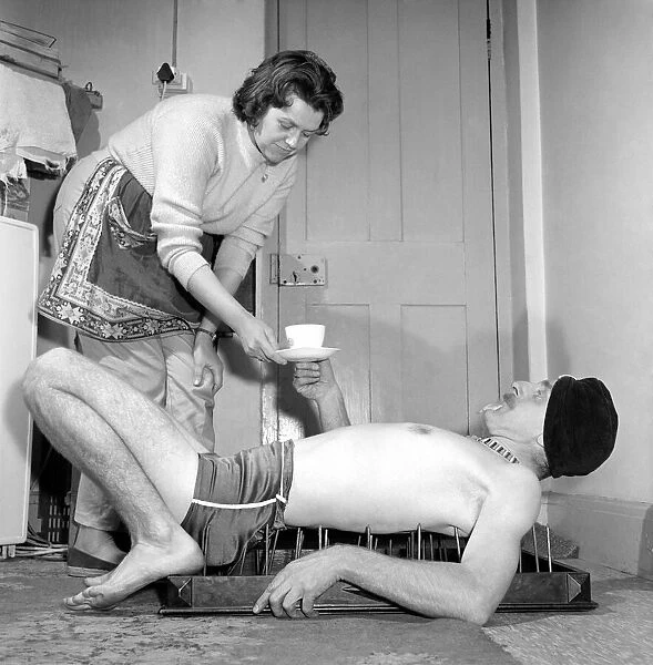 A nice cup of tea. Man laying on bed of nails accepts a cup of tea from his land lady