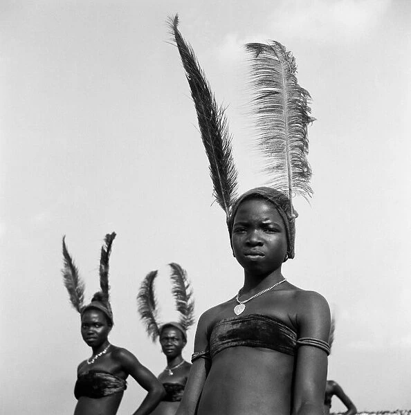 Nigerian women, wearing feathered headdresses and traditional costumes