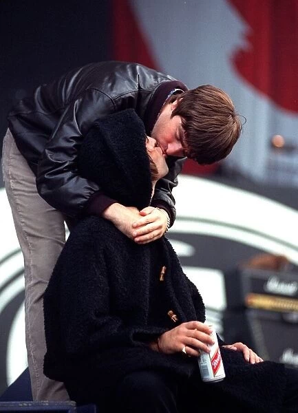 Noel Gallagher bends down and kisses his brother Liam on stage during the Oasis concert
