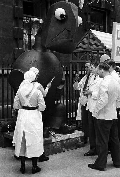 Nurses hitting a metal structure with a hammer at Barts Fair, circa 1938