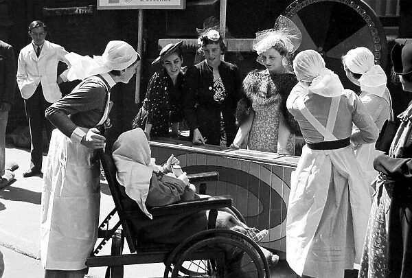 Nurses pushing a child in a wheelchair around Barts Fair, circa 1938