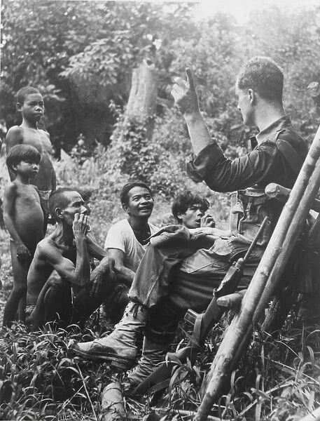 Officer leading British Army patrol stops to chat to tribesmen in Malayan jungle