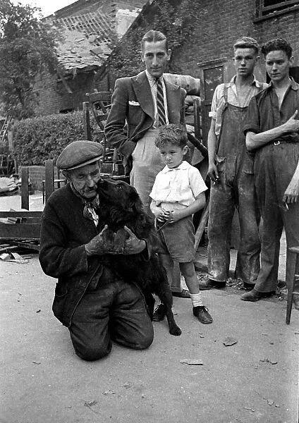A old man holds his dog as it licks his face watched by a young boy