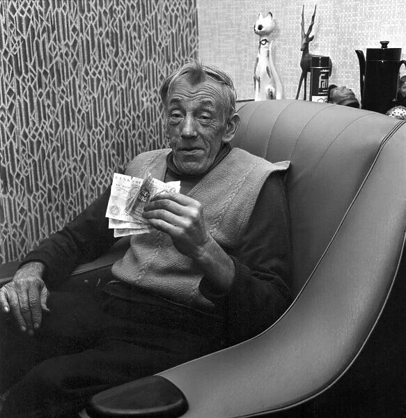 An old man sitting in his chair at home holding a bundle of money. November 1969 Z10988