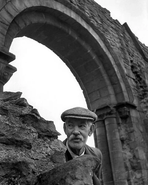 An old man wearing a flatcap peeping out from underneath an archway