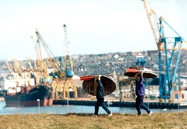 Old and new, Danny Gilchrist and Dave Potts carry thier coracles with a backdrop of