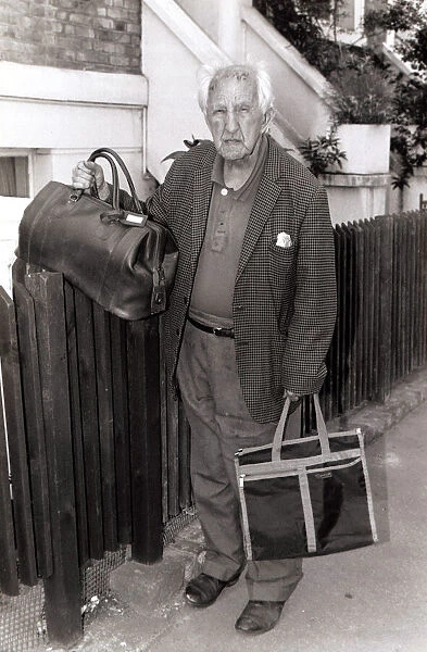 Older gentleman standing holding bags by a fence