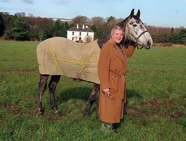 Oliver Reed actor wearing brown long coat standing in field with his horse Bobby at home