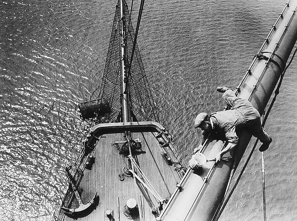 A painter painting the mast of an old sailing ship. Circa 1955