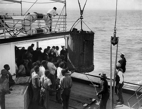 Passengers come aboard in basket owing to sea being too rough for use of companion ladder