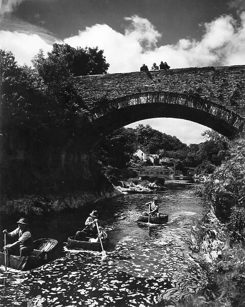 Passers-by stop on Cenarth Bridge to look at the coracle men plying their craft down