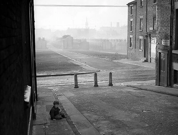 A photograph of a child sitting on the pavement in a Liverpool slum housing area