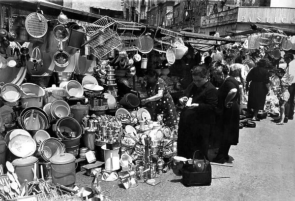 Pictured in Naples. A market scene in a suburb of Naples shows women buying kitchen ware