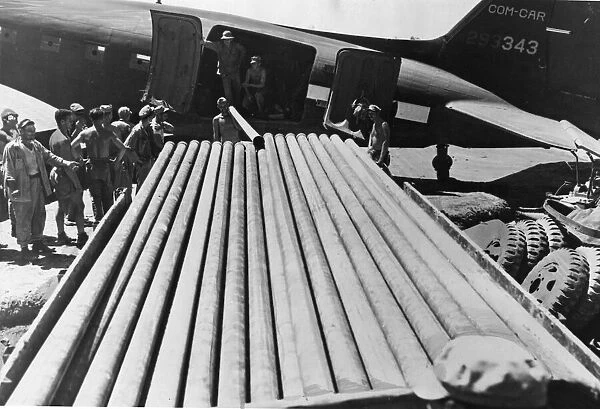 Pipes for use in constructing the long line are transferred by US soldiers from a C-47