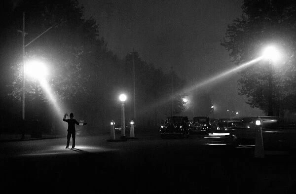 Policeman directing traffic in the fog and dark of a late autumn evening October 1958