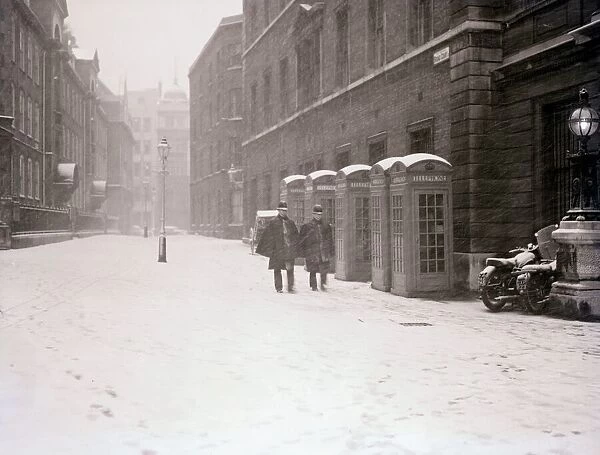 Two policeman walk down a street covered with thick snow past a row of telephone boxes