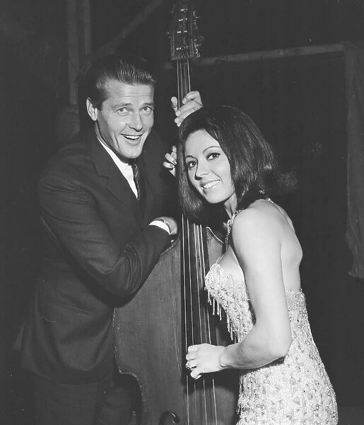 Pop singer Susan Maughan and actor Roger Moore photographed with a cello backstage during