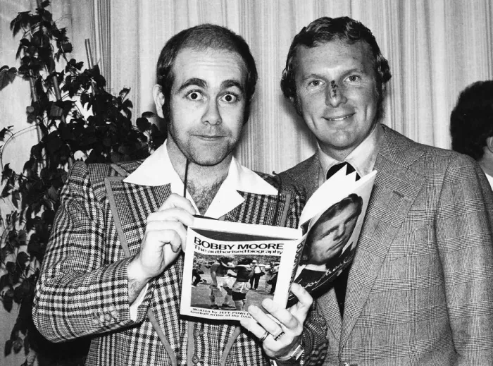 Framed Print : Pop star and chairman of Watford Football Club Elton John helps footballer Bobby Moore