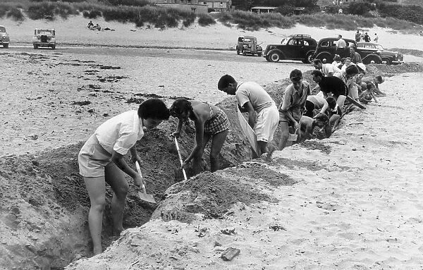 Porthcothan Bay Cornwall, 1950s Holiday Makers dig a trech in the sand to stop