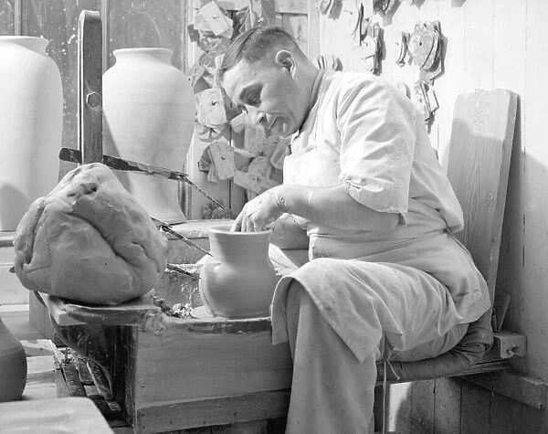 A potter sits at his potters wheel and throws a pot. Circa 1930