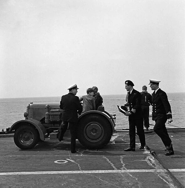The Prince of Wales is taken for a trip round the flight deck of HMS Eagle in a tractor