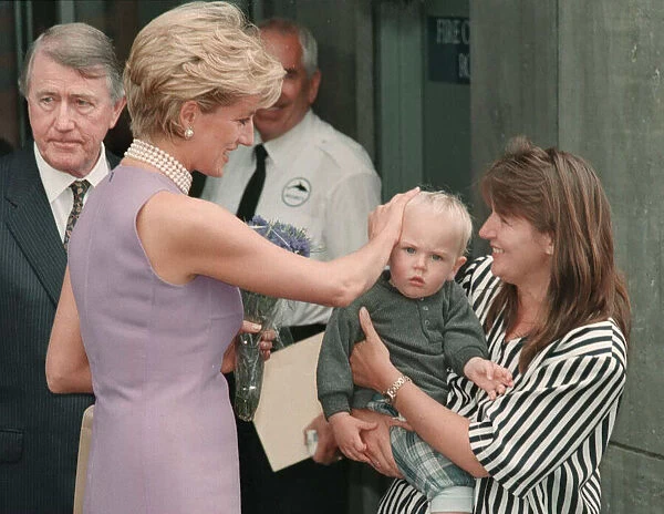 Princess Diana, wearing a purple dress and necklace greets mother a child during a