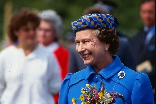 Queen Elizabeth II August 1986 holding flowers wearing a blue coat yellow blue hat on a