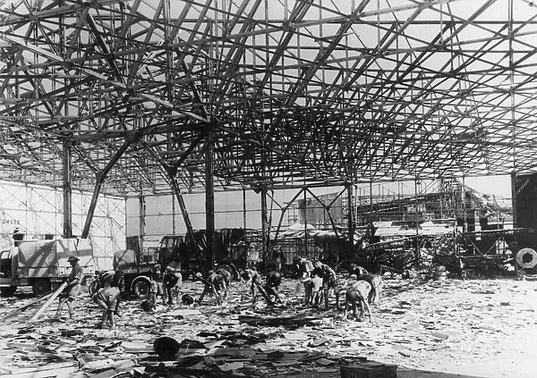 R. A. F. ground crews clear up wreckage inside a bomb shattered hanger at an airfield near