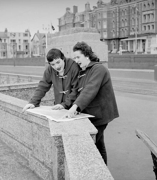 Racing drivers pat Moss and Ann Wisdom aged 21, study their map on the promenade in