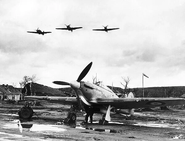 An RAF Hawker Hurricane sits on a muddy Russian airfield as Hurricanes fly overhead