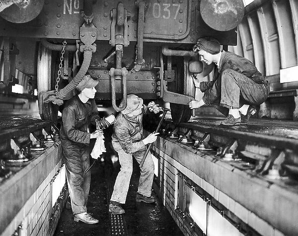 Railway inspector and women cleaners working on an engine in the floodlit pit of a train
