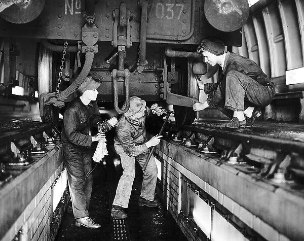 Railway inspector and women cleaners working on an engine in the floodlit pit of a train