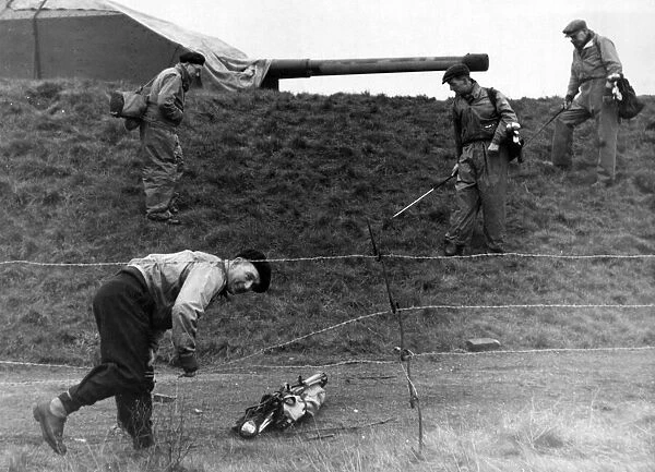 Reg Jones of Bootle climbing under barbed wire which surrounds four guns in the middle of