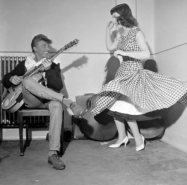 Rock and Roll singer Tommy Steele plays his guitar as girl dances for him, June 1957