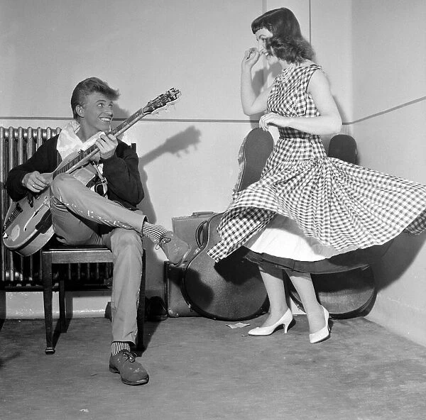 Rock and Roll singer Tommy Steele plays his guitar as girl dances for him June 1957