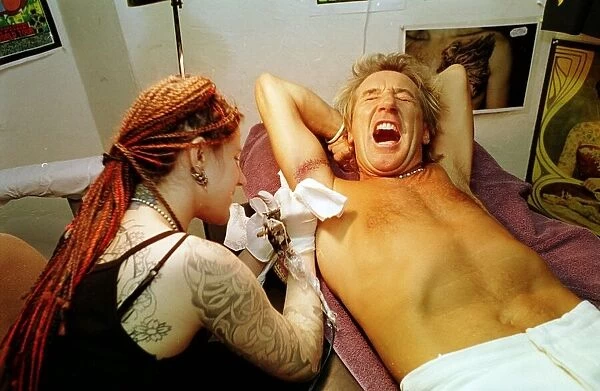 Rod Stewart grimaces in pain 21st June 1999 as tattoo artsit Ronda Hoelzer