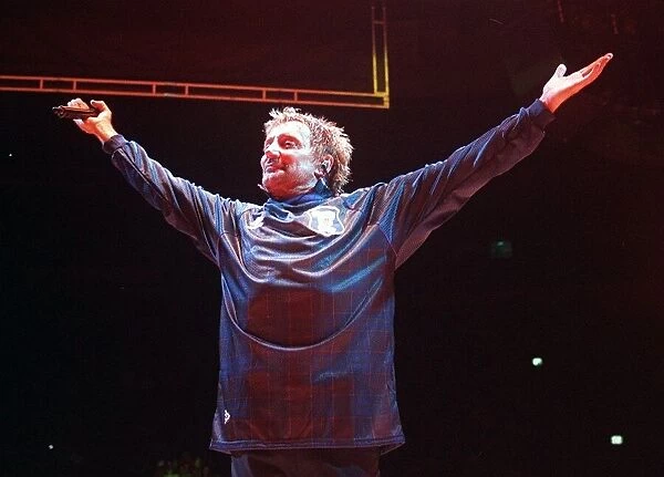 Rod Stewart pop singer wearing Scotland football jersey arms aloft holding microphone