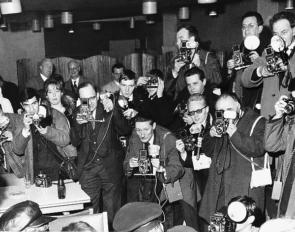 A room full of photographers take pictures of pop group The Beatles during their visit to