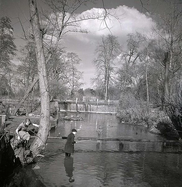 A schoolboy fishes in the Mill stream, Grove Mill near Watford Hertfordshire while his