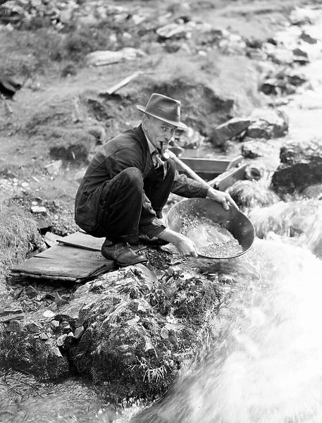 Scottish Gold Prospect, man smoking pipe by a river bank. Circa 1920