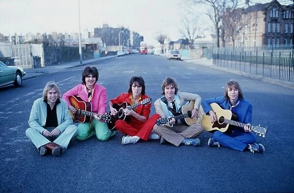 Scottish pop group The Bay City Rollers, sitting in a street holding acoustic guitars