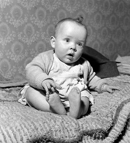 Seven month old baby girl Rosanna sitting on a bed at home March 1959