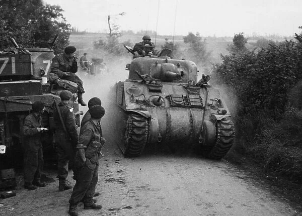 Sherman tanks pass other tanks and crew waiting for the order to advance on Caen