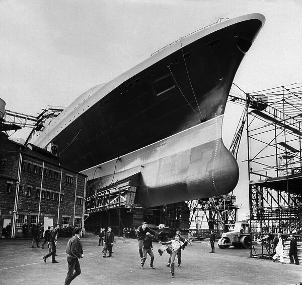 Ship builders playing football below the hull of the new Cunard Liner QE2 at Clyde