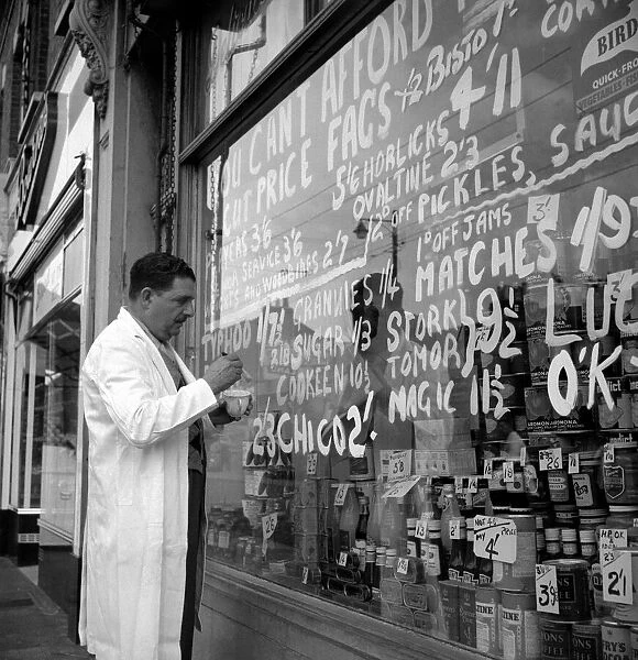 Shopkeeper putting up prices outside cut-price grocers October 1955
