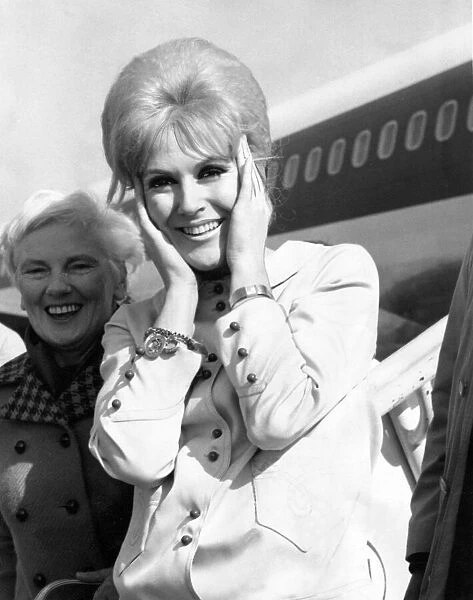 Singer Dusty Springfield holds her hair together on the tarmac of London Airport as she