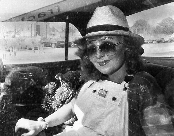 Singer Lulu in the back of a car wearing a trilby hat, sunglasses and dungarees