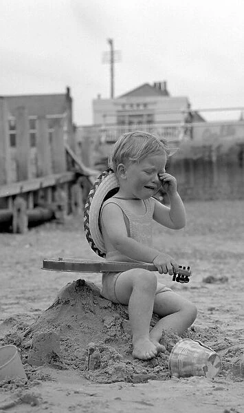 A small boy tired and over excited sitting on the remains of his sand castles crying