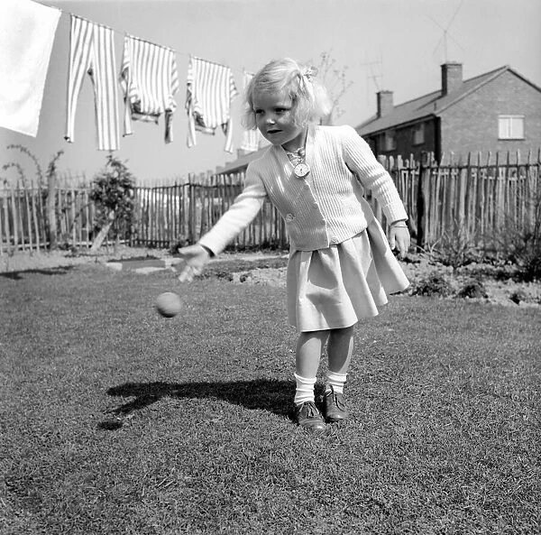 Small girl playing in the garden of her home with a ball. 1954 A228b